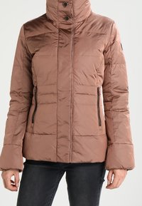 Chaqueta acolchada marrón con cuello alto, que cuenta con dos bolsillos con cremallera y una textura suave y brillante. Diseñada con una silueta ajustada y puños elásticos.