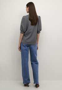 Gray puff-sleeve top, soft fabric; paired with high-waisted blue jeans. Black heels complete the outfit. Minimalistic background.