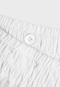 Fascia elastica bianca con texture arricciata e piccolo dettaglio con bottone rivestito in tessuto. Materiale morbido con un sottile motivo a pois.