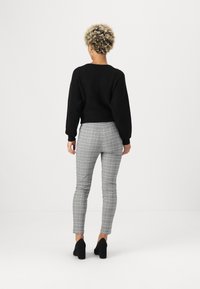 Fekete kötött pulóver bordás textúrával, szürke kockás skinny nadrággal és fekete magassarkú cipővel párosítva. Látható boka és testhez simuló fazon.