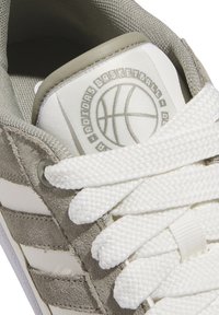 Sportowe sneakersy w białym i jasnoszarym kolorze. Zawierają teksturowane zamszowe panele, grube białe sznurówki oraz logo koszykarskie na języku.