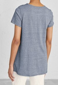 Blå kortärmad skjorta med rundad halsringning, slät textur och diskreta sömnadsdetaljer. Hemsömnaden är något rundad bak.