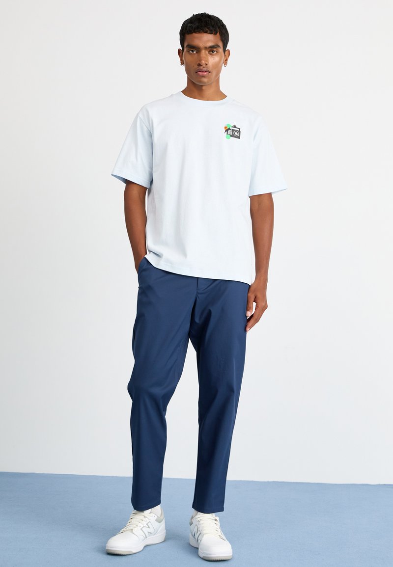 Camiseta de algodón de color azul claro con mangas cortas, con un diseño gráfico en el pecho, combinada con pantalones marinos y zapatillas blancas.