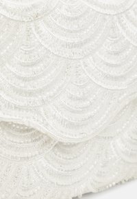 Bílá perlová kabelka s vlnitým vzorem a texturovaným povrchem, s jemným leskem a propracovanými stehy po celém povrchu.