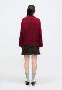 Burgundská pletená svetr s volným střihem, ribovaným lemem, spárovaný s tmavě hnědou semišovou sukní, šedými ponožkami a černými botami s kovovými akcenty.