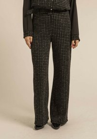 Pantalons larges à carreaux noir et blanc, en tissu texturé, taille haute, avec un bouton avant et un détail de ceinture, associés à des chaussures noires.