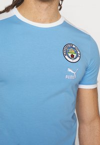 Svetle modré tričko Manchester City F.C. s bílým límcem a manžetami, s klubov ým znakem a bílým logem Pumy na hrudi.