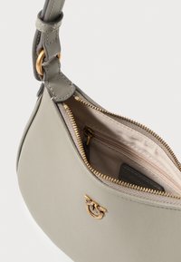 Svetlošedá kožená kabelka so zlatým zipsom, zakrivený tvar a hladká textúra. Obsahuje malú vnútornú kapsu a akcent loga.