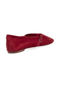 Zapato plano de ante rojo con puntera afilada y una delgada correa en el tobillo que lleva una hebilla metálica. Suela plana y silueta sencilla.