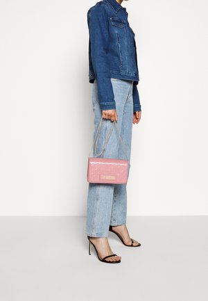 Růžová kabelka z lakované kůže s řetízkovým popruhem, obdélníkový tvar, reliéfní vzor. Nositelná s modrou džínovou bundou a světlými džíny, doplněná černými podpatky.