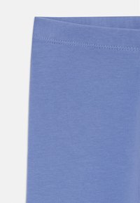 Leggings bleu clair avec une texture lisse et une large ceinture cousue. Le tissu semble extensible et doux, sans motifs visibles.