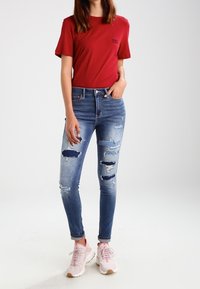 Červené bavlněné tričko, modré roztrhané skinny džíny s mnoha dírami a světle růžové tenisky s bílou podrážkou.