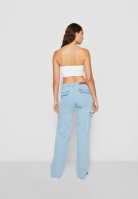 Pantalons cargo bleu clair avec une coupe décontractée, présentant des poches arrière et des rabats latéraux. Associés à un top court blanc.