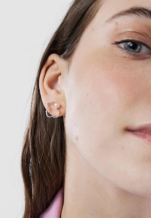Orecchini d'argento a forma di contorno ondulato con un piccolo accento di perla tonda. Vista ravvicinata sull'orecchio e sul collo.