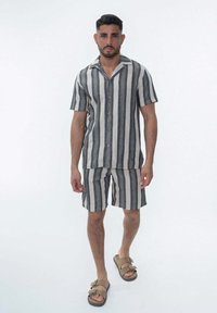 Ensemble en tissu rayé gris et crème composé d'une chemise à manches courtes et d'un short. Il dispose d'une fermeture à boutons et d'un col plat. Porté avec des sandales marron.