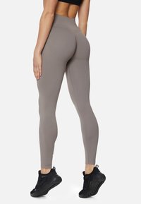 Leggings a vita alta, aderenti, in un morbido tessuto grigio con una texture liscia, caratterizzati da dettagli di cucitura discreti e abbinati a sneakers nere.