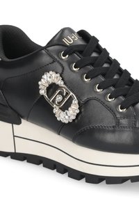 Czarne skórzane sneakersy z grubą białą podeszwą, ozdobione złotymi elementami i detalem logo wysadzanym kryształami po bokach. Czarne sznurówki.