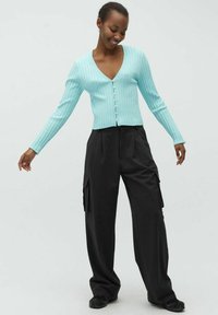 Helles blauer Rippstrick-Cardigan mit langen Ärmeln, V-Ausschnitt und Knopfverschluss, kombiniert mit lockeren schwarzen Cargo-Hosen mit Seitentaschen.