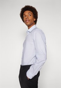 Helles blaues Hemd mit strukturiertem Finish, langen Ärmeln und klassischem Kragen. Kombiniert mit schwarzen Hosen.