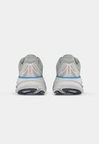 Tênis atléticos cinzentos com um cabedal texturizado, detalhes em azul e laranja, e uma sola branca espessa. Apresenta um salto significativo e um design acolchoado.