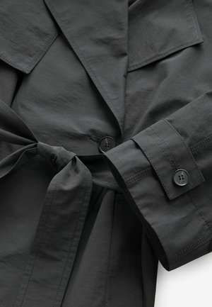 Sort, let trøje med bånd i taljen, store lommer og knapmanchetter, med en glat tekstur og strømlinet design.