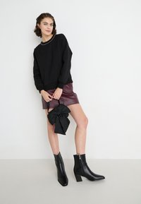 Felpa nera con scollatura strutturata, mini gonna in pelle bordeaux e stivali neri alla caviglia con borsa in tessuto testurizzato dotata di un fiocco.