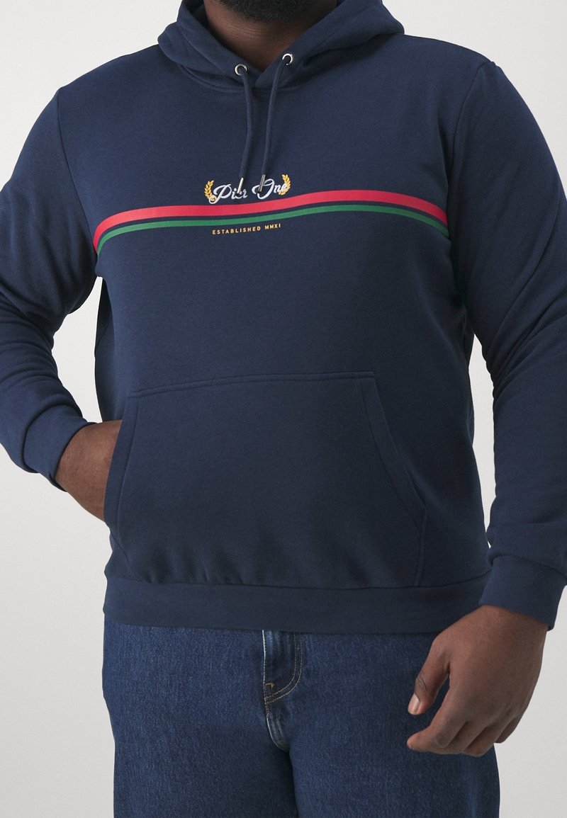 Sudadera color azul marino hecha de un tejido suave, con un bolsillo canguro en la parte delantera, capucha con cordón y detalles decorativos a rayas en rojo y verde.