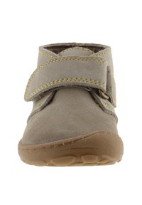 Bota de tobillo de ante gris con una correa de velcro, acentos de costura amarilla y una suela de goma con patrones de dibujo circular.