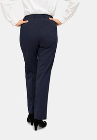 Maßgeschneiderte navyblaue Hosen mit einem dezenten Karomuster, einer taillierten Taille und Faltendetails, kombiniert mit schwarzen hohen Schuhen.