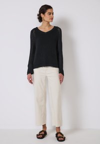 Maglione nero a maglia con maniche lunghe, scollo a V e polsini a costine, abbinato a pantaloni beige a gamba larga e sandali neri con una fascia decorata.