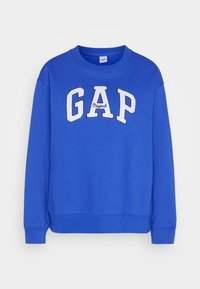 Sudadera azul de algodón, con un logotipo blanco bordado de "GAP" en el frente y puños y dobladillo acanalados. Diseño simple y cuello redondo.