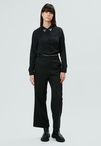Camisa negra de botones con cuello decorado, combinada con pantalones negros de pierna ancha y botas negras gruesas. Diseño minimalista, textura de tela suave.
