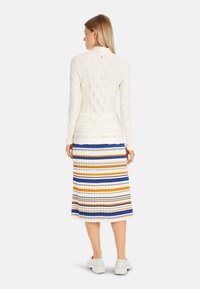 White textured long-sleeve top and a pleated midi skirt with horizontal stripes in blue, orange, and white. Plain white sneakers complete the look.