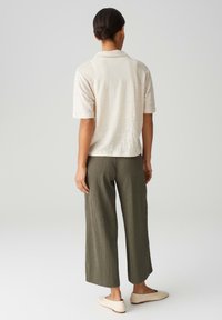 Polo shirt beige clair à manches courtes en tissu texturé, associé à un pantalon large côtelé vert olive et des chaussures slips crème.