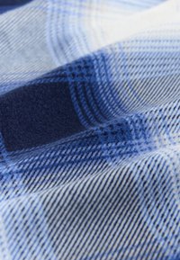Tissu doux avec un motif à carreaux bleu et blanc présentant de grands et petits carrés, montrant la texture et les plis.