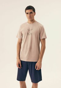 Jasnoróżowa bawełniana koszulka z krótkim rękawem i czarnym nadrukiem, zestawiona z granatowymi szortami z delikatnym wzorem kropek.