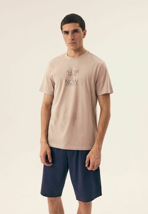 Helles rosa Baumwoll-T-Shirt mit kurzen Ärmeln und schwarzem Drucktext, kombiniert mit navyblauen Shorts mit einem dezenten Punktmuster.