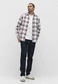 Ternede flanelskjorte med hvide, røde og blå tern, lagt over en hvid T-shirt. Mørkeblå jeans og beige sneakers fuldender outfittet.
