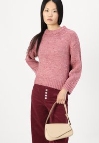 Maglione rosa lavorato a maglia con scollo rotondo e finitura testurizzata, abbinato a pantaloni in corduroy bordeaux con bottoni argentati. Borsa color beige.