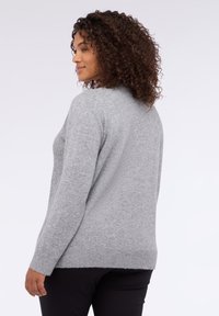 Šedý pletený svetr s dlouhými rukávy, kulatým výstřihem a žebrovaným lemem. Měkká textura a volný střih, nošený přes černé kalhoty.