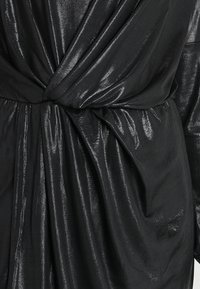 Schwarzes Kleid aus einem glänzenden, strukturierten Stoff mit einem Wickeldesign und Knotendetails an der Taille, die drapierte Stoffabschnitte erzeugen.