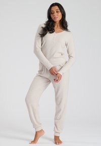 Conjunto de loungewear en un suave color beige claro, que incluye una blusa de manga larga con cuello en V y detalles de botones, acompañada de pantalones relajados y ajustados.