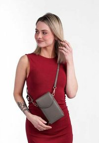 Křížová taška z šedé kůže, obdélníkového tvaru s klopovým zapínáním, nastavitelným popruhem a jemným detailem s logem. Nesená na osobě.