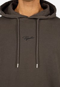 Brauner Hoodie mit Kordelzügen, ausgestattet mit einem aufgestickten Logo auf der Brust. Hergestellt aus weichem Stoff, mit lockerer Passform und gerippten Bündchen.