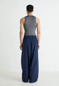 Athletic outfit featuring a fitted gray tank top with a round neckline and loose navy blue pants with an elastic waistband and side stripes.