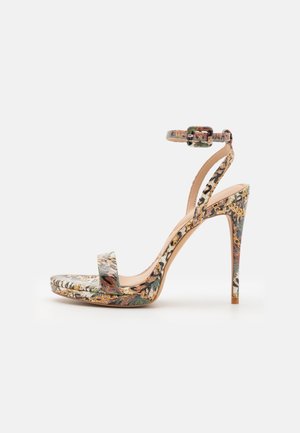 Sandale à talon haut avec bride à la cheville, bout ouvert, et motif floral et chaîne dans des tons beige, vert et marron sur fond blanc.