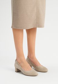 Beżowe zamszowe szpilki na słupku z okrągłymi noskami i niskim wycięciem; gładka faktura i minimalistyczny design.