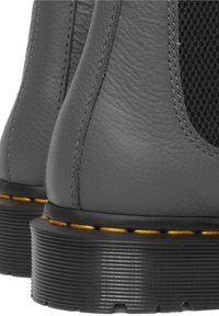 Gros plan de bottes en cuir noir avec coutures jaunes et semelles en caoutchouc épaisses à rainures.