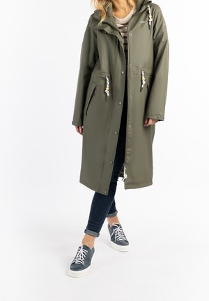 Olijfgroene waterdichte jas met een capuchon, voorzien van witte trekkoorden, een ritssluiting aan de voorkant en zijzakken, gedragen over donkere jeans en grijze sneakers.