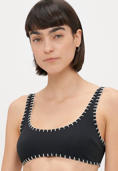 Svart bikinioberdel med firkantet halslinje, som har kontrasterende hvit søm langs kantene og stroppene. Glatt tekstur, minimalistisk design.